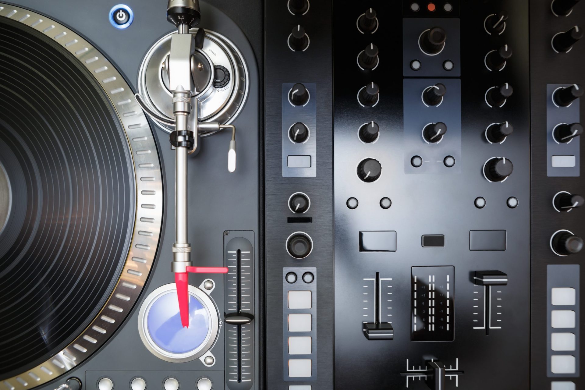 DJ-Plattenspieler mit Tonarm und rotem Nadelschliff neben Mischpult mit Reglern und Schiebereglern