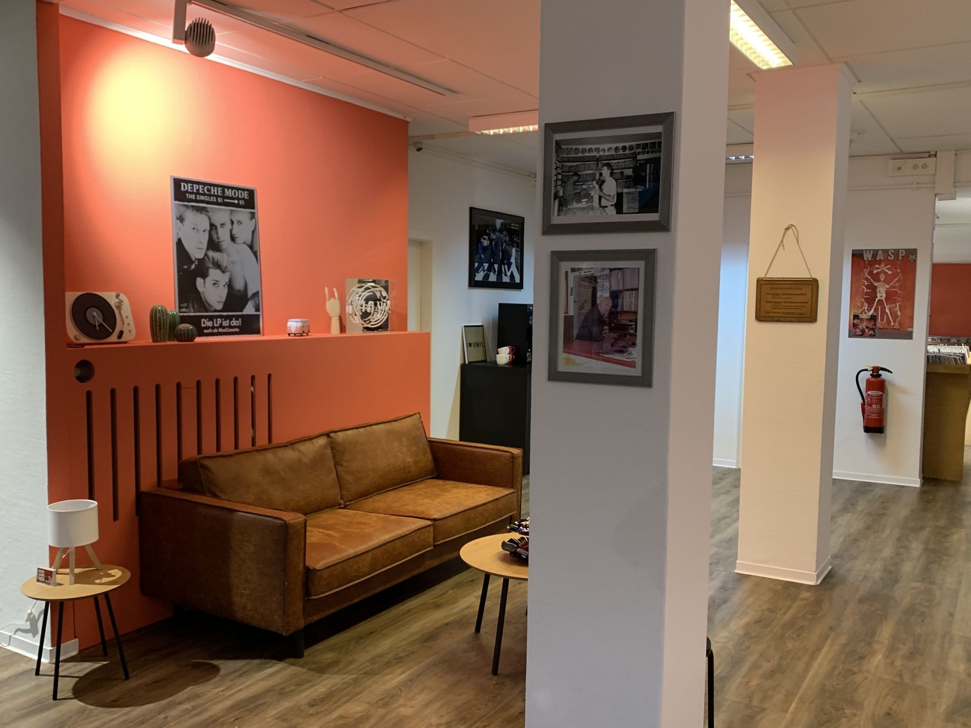Braunes Ledersofa vor orangefarbener Wand mit Depeche Mode Poster und Schallplatten im Wohnzimmer