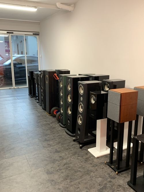 Mehrere Lautsprecher verschiedener Größen und Designs in einem Raum, aufgereiht an einer Wand mit Fenster im Hintergrund