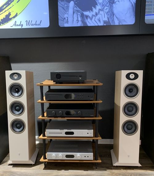 Zwei weiße Standlautsprecher neben einem Holzregal mit fünf schwarzen und silbernen Audio-Komponenten