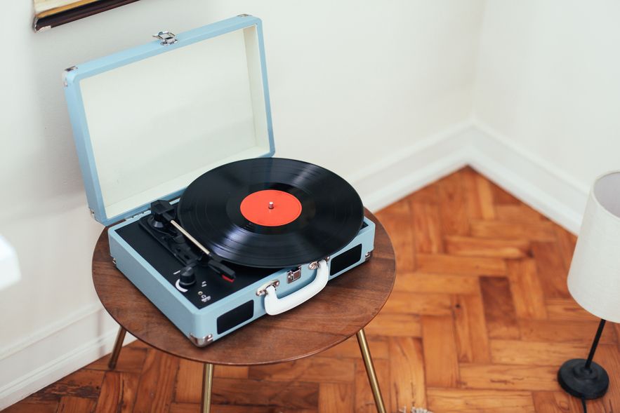 Blauer tragbarer Plattenspieler mit schwarzer Schallplatte auf rundem Holztisch in einem Raum mit Parkettboden